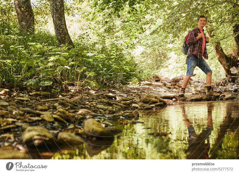 Trekking with backpack concept image. Backpacker in trekking boots crossing mountain river. Man hiking in mountains during summer trip adventure travel vacation