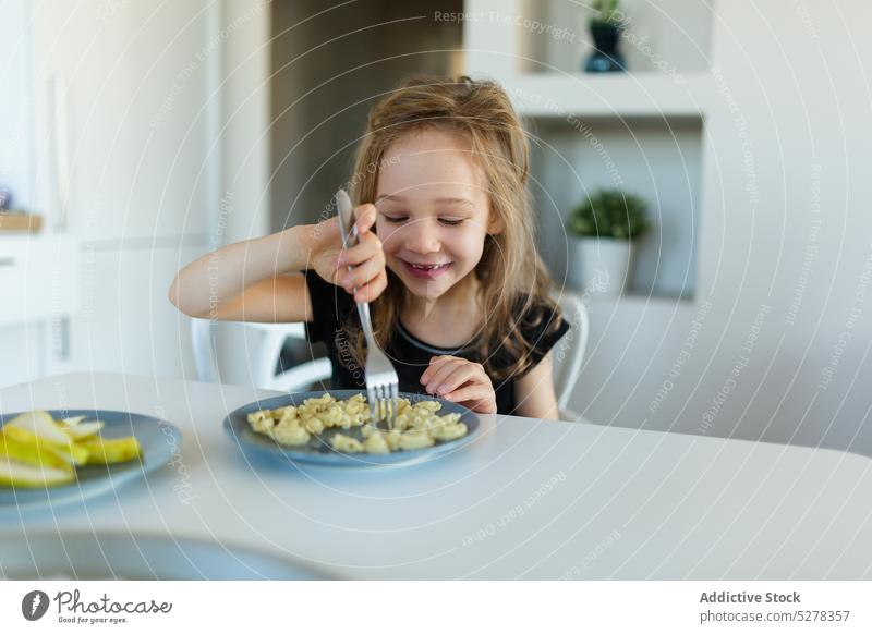 Happy preschool girl eating pasta at table child nutrition nourish smile food kid happy nutrient childhood plate content cute lunch charming dish appetite