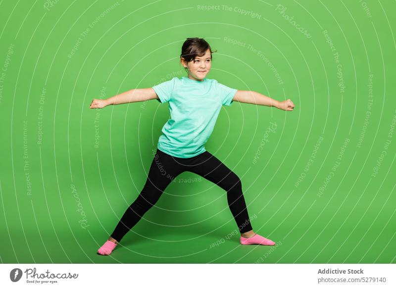 Cheerful girl exercising in studio kid child smile positive yoga practice warrior pose sportswear colorful vivid fitness asana healthy flexible wellness