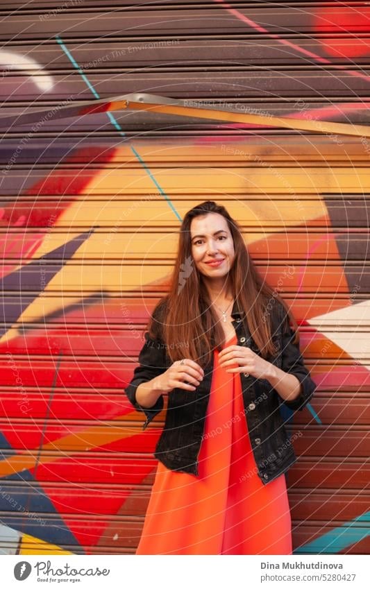 candid photo of a young woman standing in front of a graffiti wall city Graffiti art Lifestyle portrait one young woman solo alone red red dress casual casually