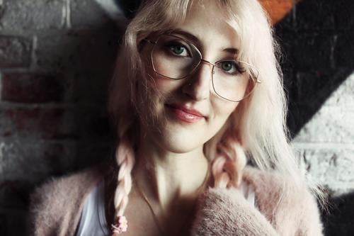 Young woman with pink blonde hair stands smiling in front of brick wall defaced with graffiti Woman Brick Wall (building) Graffiti portrait Eyeglasses pretty