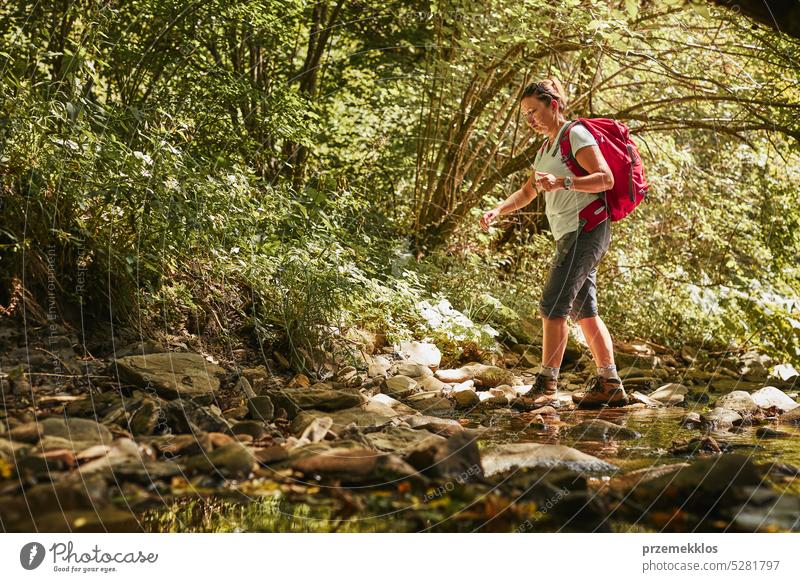 Traveling with backpack concept image. Backpacker female in trekking boots crossing mountain river. Summer vacation trip adventure travel hiking landscape
