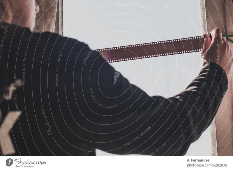 A woman holding a strip of 35mm analogue film negatives backlit in a window. Analog photography film photography analog film Photography Film 35mm film