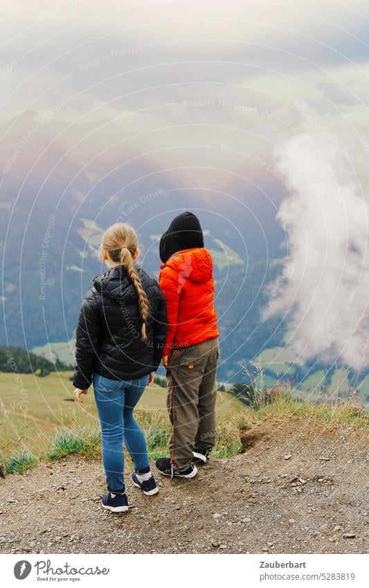 Two children in back view standing on a mountain and looking down to the valley Rear view Couple Valley Clouds Hiking hike Nature Landscape Infancy Happy Amazed