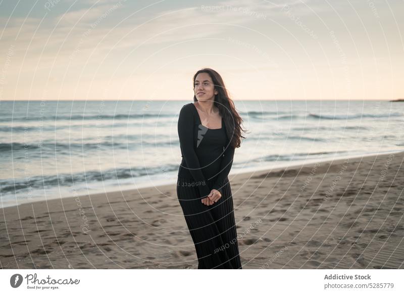 Self assured ethnic lady standing on sandy seashore and smiling woman beach smile tourist sunset vacation confident feminine dance happy female young hispanic