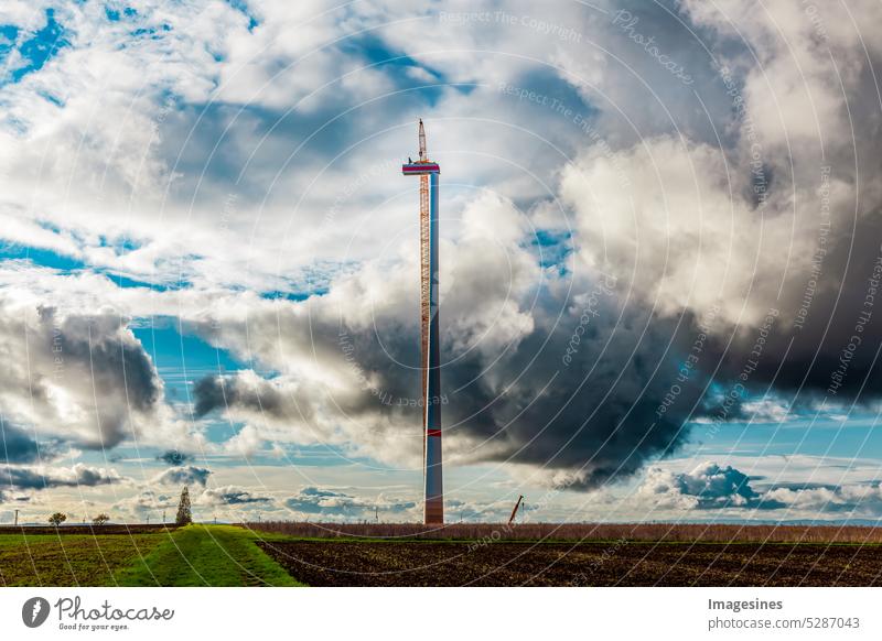 Thunderstorm. Construction and assembly of a wind turbine by crane and dark clouds are gathering, farmland with construction work for wind turbines in the wind farm. Thunderclouds moving in. Wörrstadt, Germany.