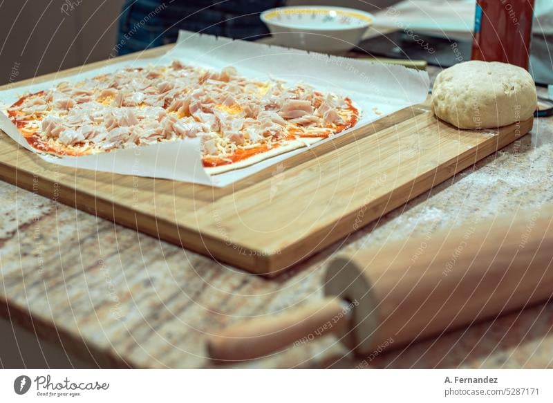A homemade ham and cheese pizza on a wooden board next to a rolling pin. Concept of preparation of pizzas at home homemade food Homemade pizza Pizza
