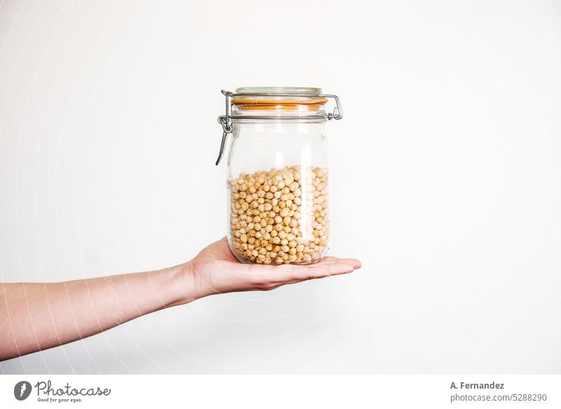 Detail of a hand holding a glass jar full of chickpeas. Concept of sustainable food storage in the home cupboard. Chickpeas Preserving jar Food Storage