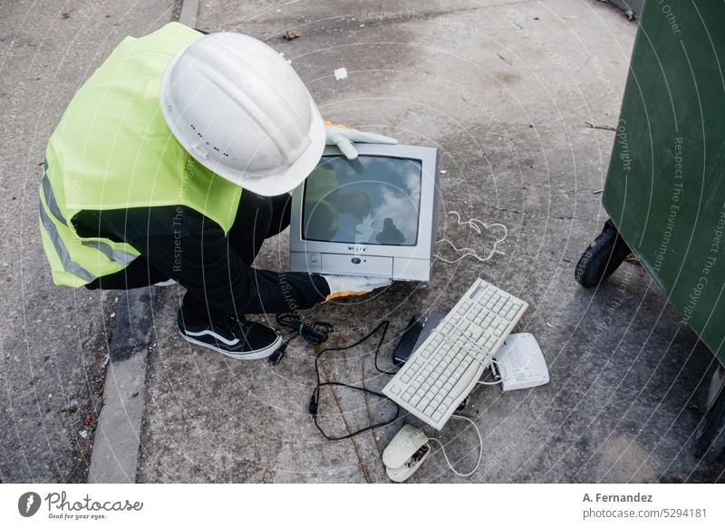 A worker at a recycling center collecting an old television amongst a broken keyboard and computer mouse. Technology recycling concept. Waste management