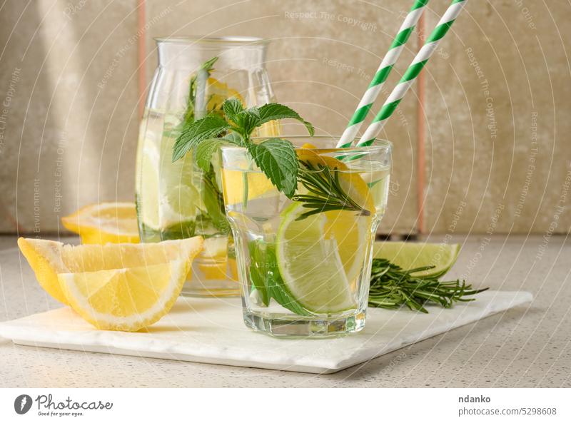Lemonade in a transparent glass with lemon, lime, rosemary sprigs and mint leaves on a white background lemonade drink cocktail refreshment fruit ice green