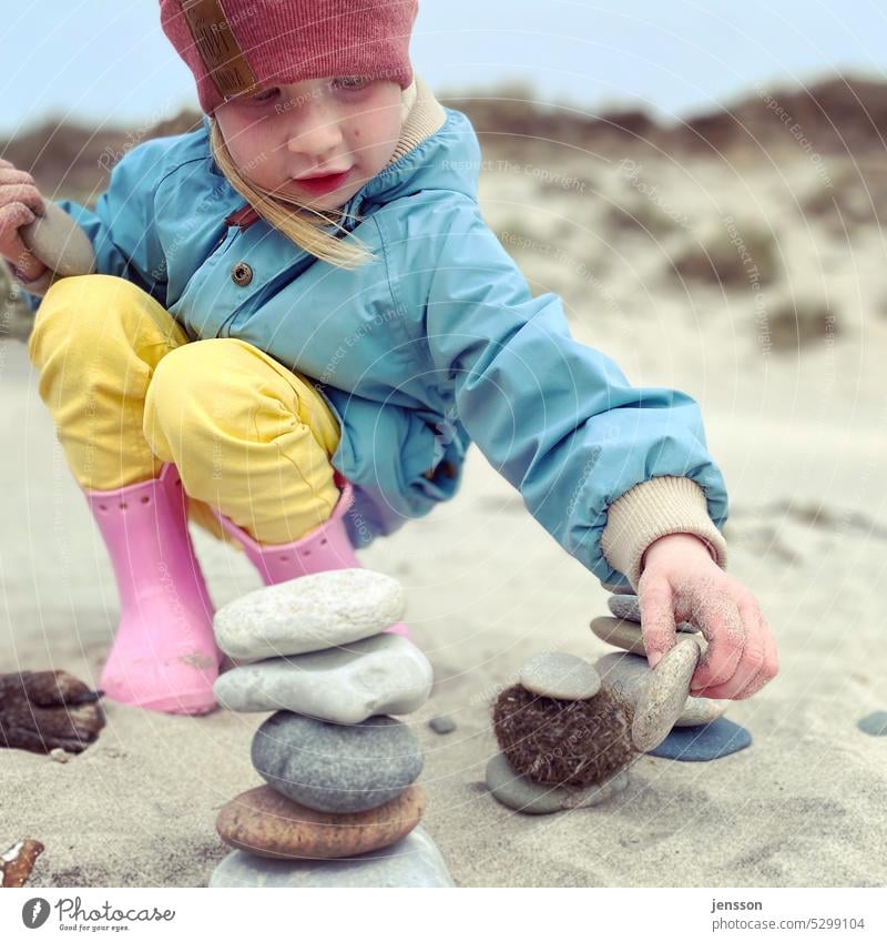 A little girl playing with stones on the beach variegated pink Yellow light blue Beach Pink Rubber boots Child Infancy Childlike Playing Exterior shot