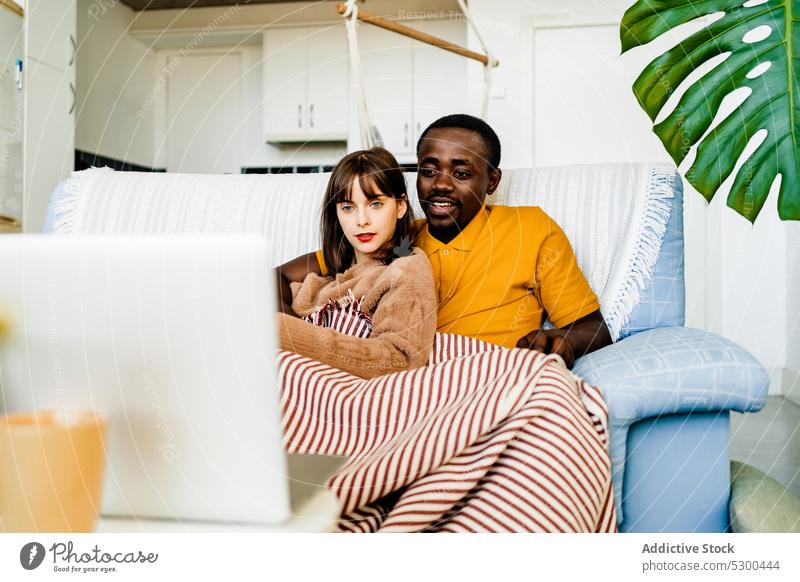 Couple using laptop in living room at home couple sofa relationship browsing together spend time diverse online multiracial multiethnic young internet device