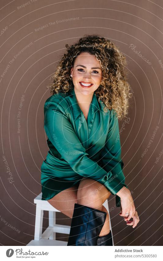 Smiling female sitting on chair in studio woman model gorgeous curly hair makeup appearance studio shot personality glance positive cheerful smile cosmetic lady