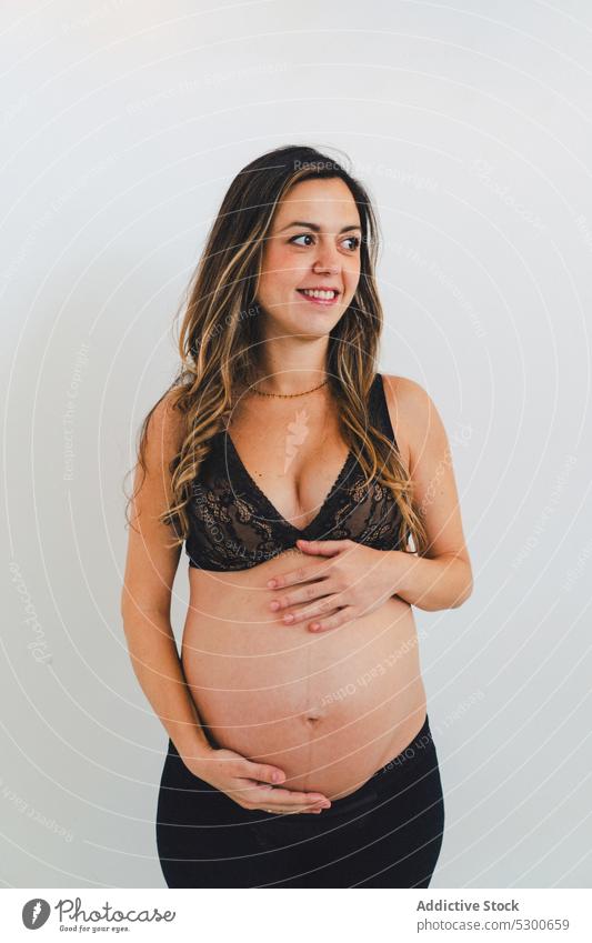 Young smiling woman carrying baby standing against white background pregnant studio shot happy maternity leave care smile love await glad caress delight