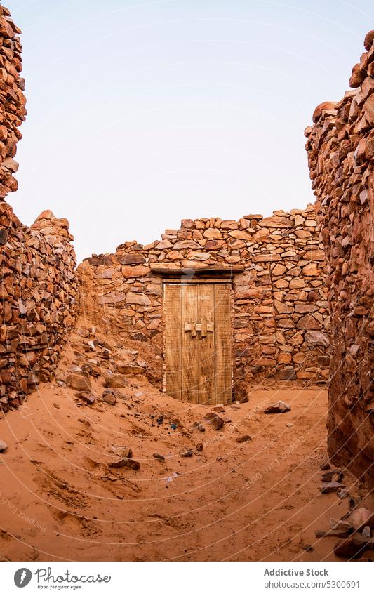 Old weathered wooden door in stone wall shabby abandoned old damage building rocky aged destroy sahara mauritania africa broken destruct forgotten worn out