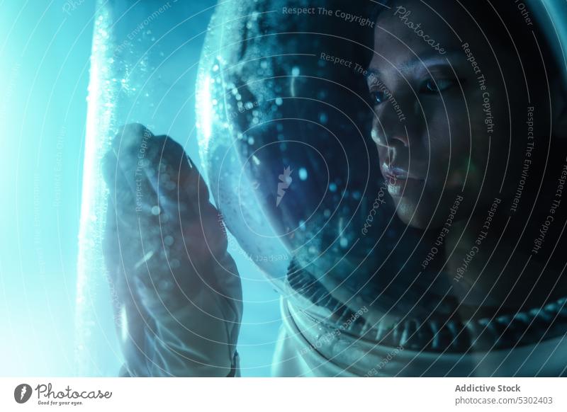 Dreamy woman in cosmonaut suit looking at glass astronaut helmet pensive window model transparent neon fashion futuristic young thoughtful style female serious