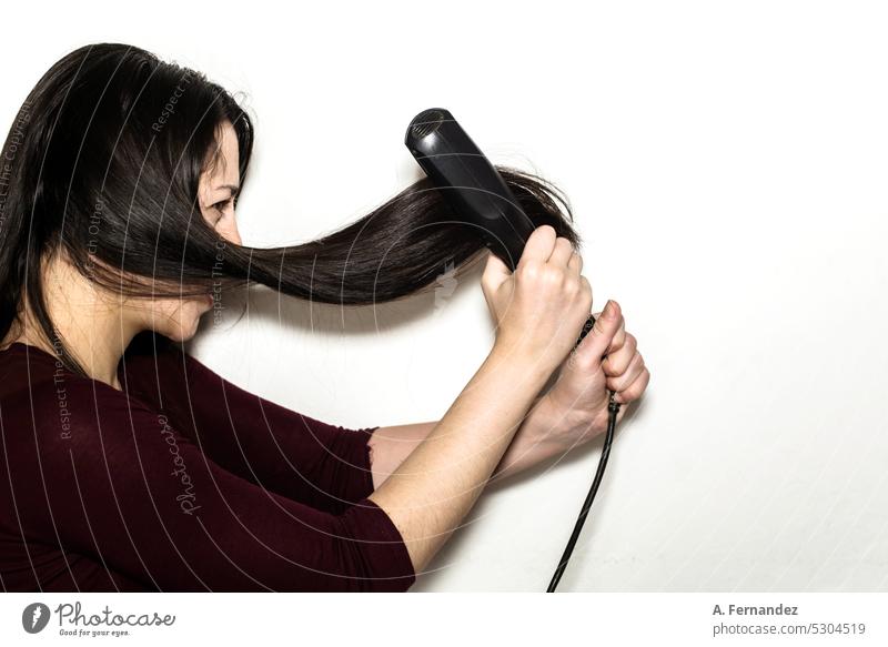 A woman holding tightly and furiously hair straighteners on a white background. Concept of damage due to continued use of heat on the hair. iron hair hair iron
