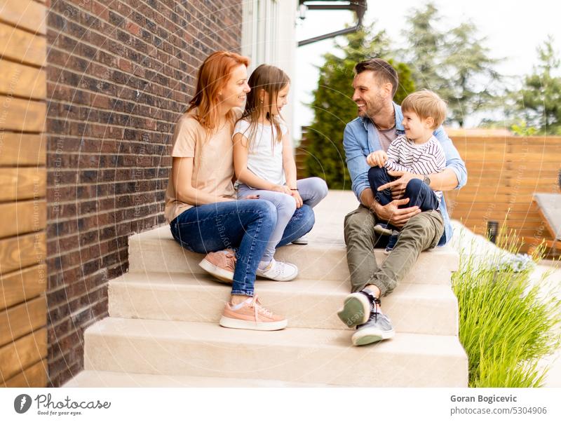 Family with a mother, father son and daughter sitting outside on the steps of a front porch of a brick house parent stairs girl child kid happiness childhood