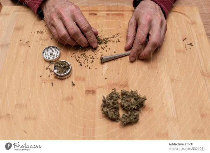 Crop man adding dried cannabis in marijuana grinder weed joint smoke drug prepare ganja cannabinoid herb natural cbd leaf legalize table make narcotic hemp