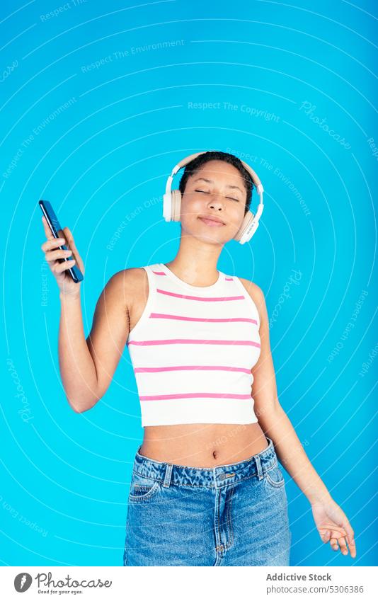 Cheerful ethnic woman listening to music on headphones and dancing dance smartphone audio song playlist smile excited cheerful happy young casual stripe top