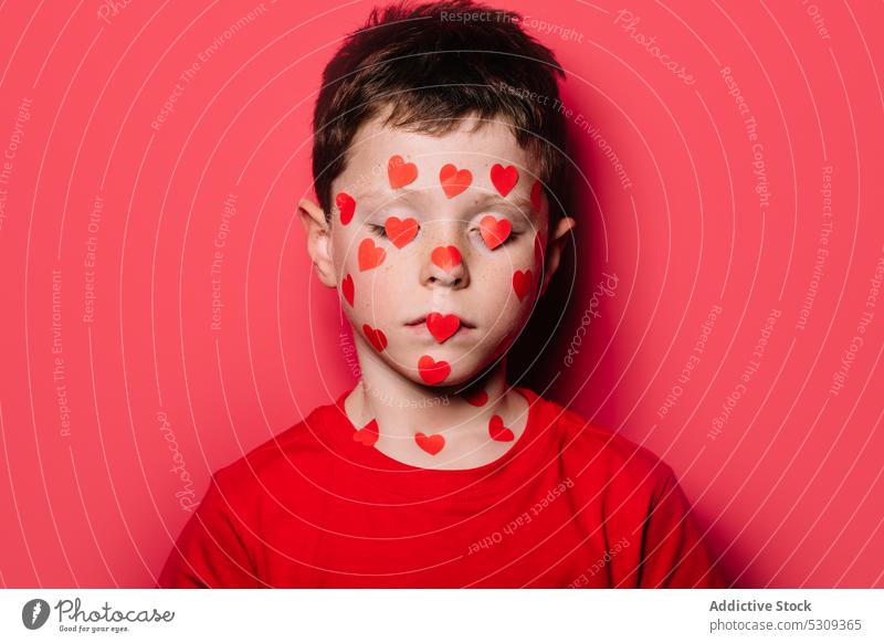 Anonymous cute boy in red casual shirt with red love sticker on face while  posing for photograph - a Royalty Free Stock Photo from Photocase