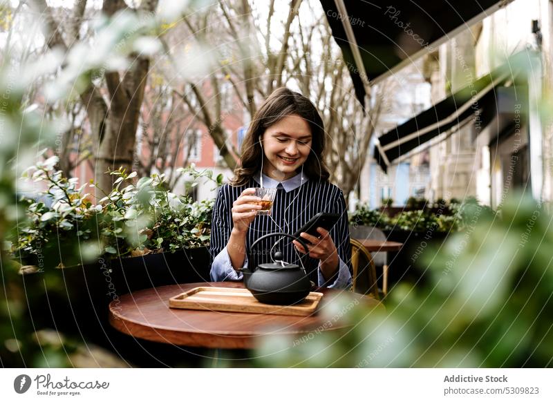 Woman using smarthone on cafe terrace woman smartphone positive headphones watch tea teapot mobile phone online internet female device gadget breakfast smile