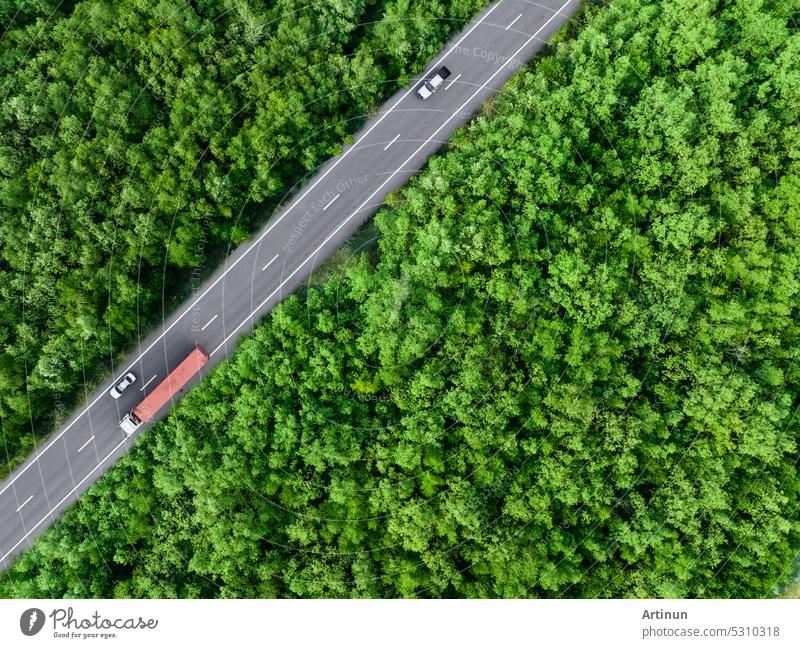 Aerial top view of car and truck driving on highway road in green forest. Sustainable transport. Drone view of hydrogen energy truck and electric vehicle driving on asphalt road through green forest.