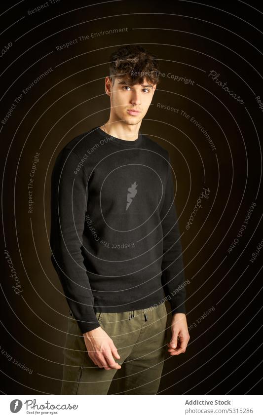 Teen boy standing against dark brown background man portrait style appearance individuality young friendly curly hair teen teenage casual sweatshirt brunet