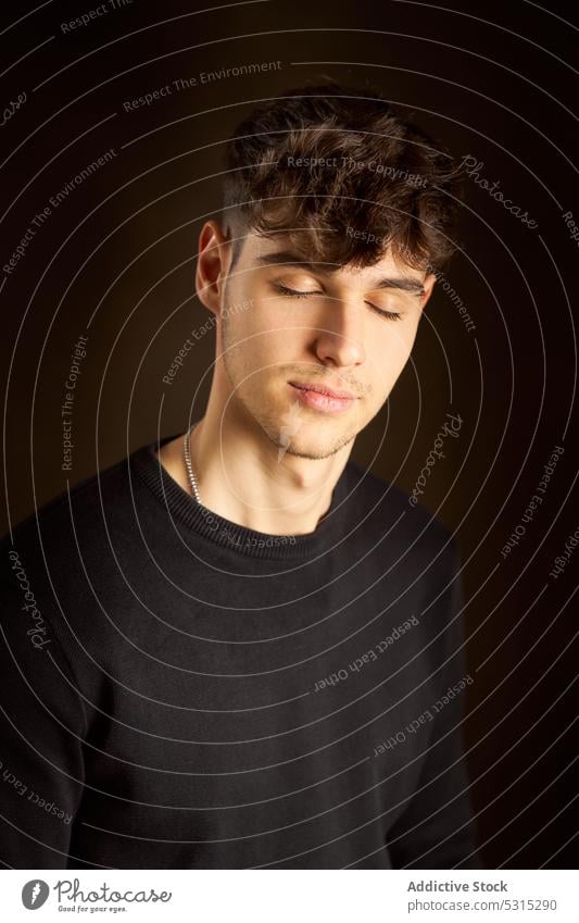 Calm teenager with closed eyes in dark room man eyes closed calm appearance curly hair portrait individuality tranquil personality serene male style young
