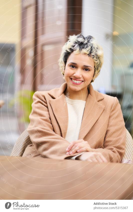 Smiling woman in coat at table on street cafe smile positive cheerful trendy rest terrace female happy young wooden cafeteria enjoy modern delight chill