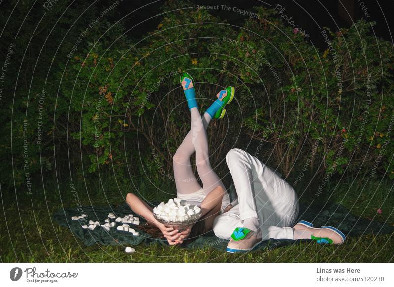 A fashionable couple is having a picnic with some muffins. Dressed in white they’re feeling romantic. And the accent is colorful shoes. Green ones. Pink ones. Avant-garde style. Getting wild in green bushes on a hot summer night.