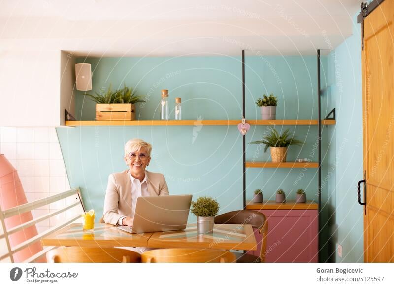 Senior woman using mobile phone while working on laptop and drinking fresh orange juice in the cafe aged call coffee coffee shop coffeehouse communication