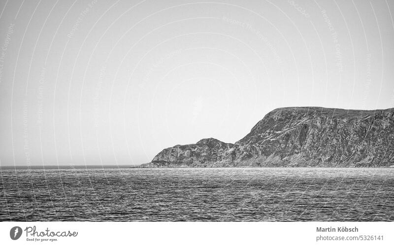 View from the sea to the West Cape in Norway in sunshine in black and white. Western Cape. Fjord ocean atlantic waves sky cloud landscape mountain calm blue