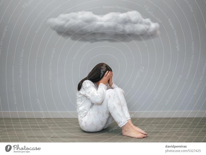 Woman with mental health problems covering her face with hands under a dark cloud unrecognizable desperate woman anxiety sad disorder depression sitting floor