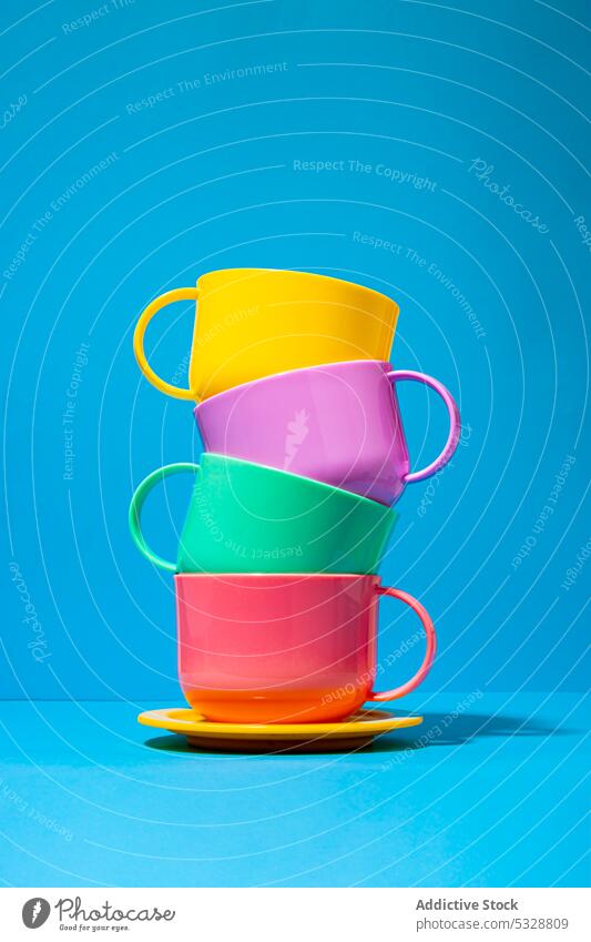 Multicolored ceramic cups on blue background saucer mug stack tower colorful bright composition shape table design porcelain dishware creative set minimal vivid