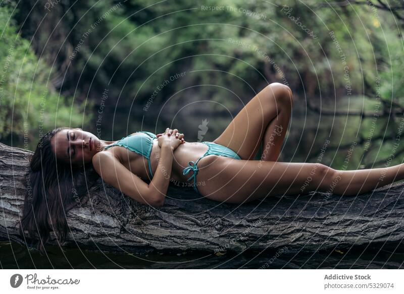 Slim woman in bikini lying on tree trunk lake rest nature dreamy swimsuit swimwear female young summer fit water serene recreation vacation slim peaceful