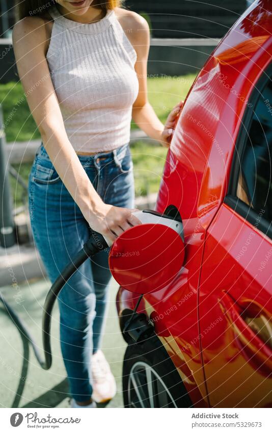 Woman charging electric car in station woman charge driver automobile plug insert transport energy young casual female power modern battery connection cable