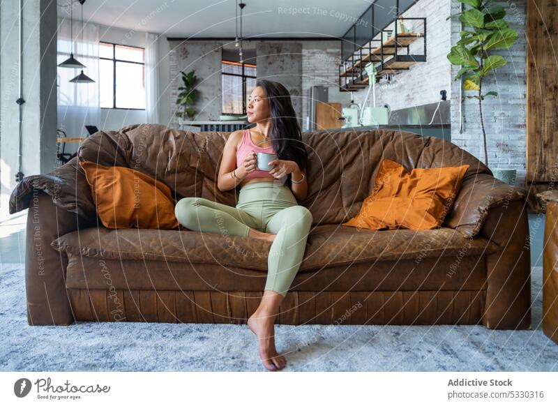 Relaxed woman drinking coffee on sofa in cozy room rest hot drink home comfort relax living room casual young cup lifestyle female couch tea chill asian ethnic