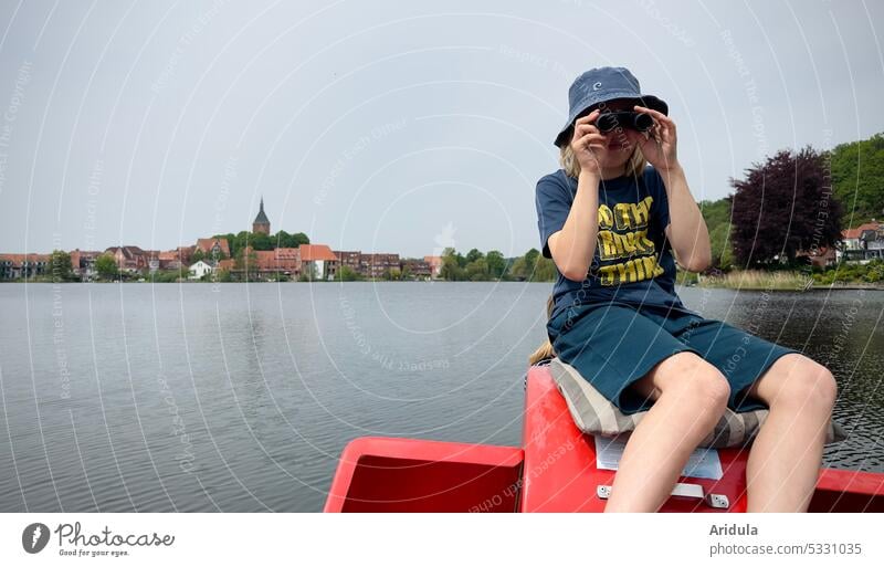 Child sitting on pedal boat on lake looking through binoculars, small town with church tower in background Boy (child) Binoculars Lake Water Pedalo Town moelln