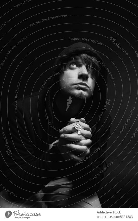 Young man praying in studio clasped hands religion hope symbol worship young god faith spiritual folded male calm tranquil serene peaceful casual guy wish