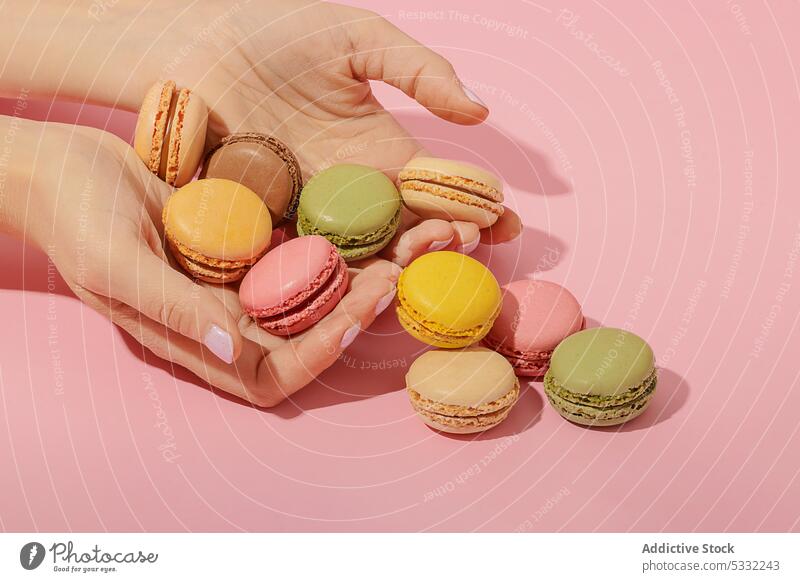 Crop woman grabbing macaroons on pink background dessert sweet colorful delicious tasty food treat snack yummy sugar confectionery multicolored pastry female