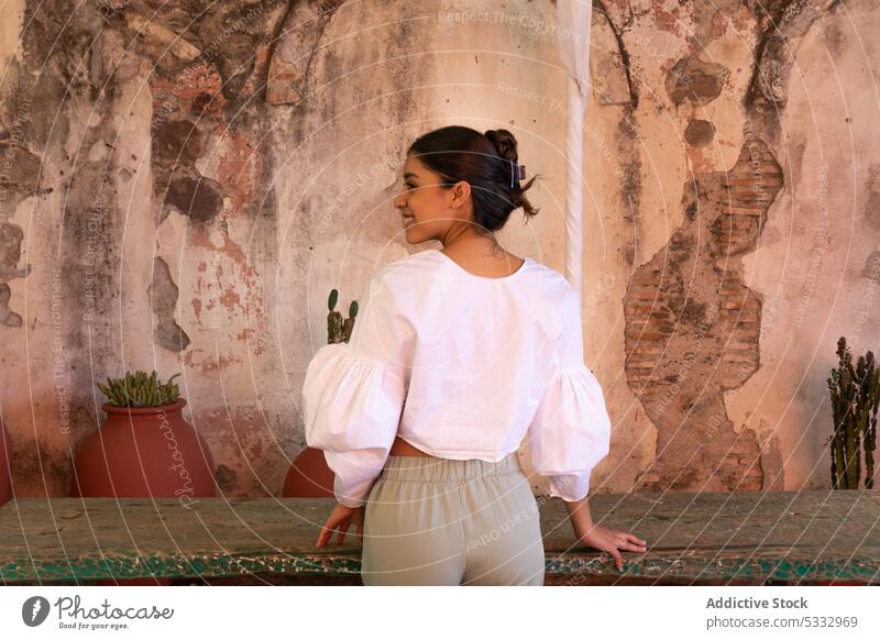 Back view of woman in stylish clothes standing near table by old building style smile pot cathedral natural visit positive plant wood green wooden glad young