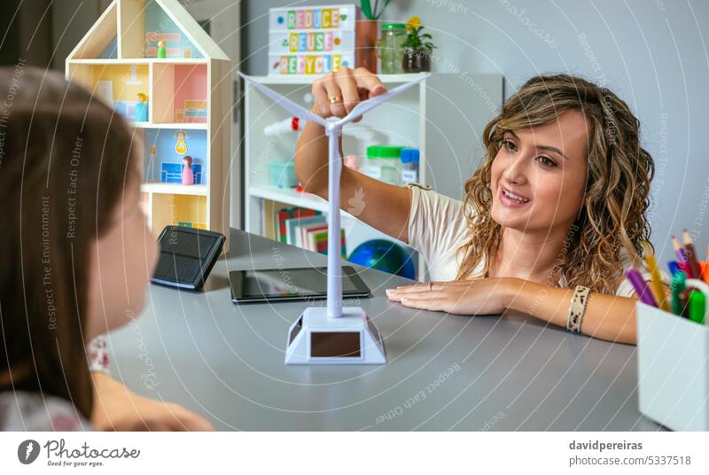 Teacher showing windmill to schoolgirl in ecology classroom female teacher portrait solar renewable energy student education smile happy pointing finger blade