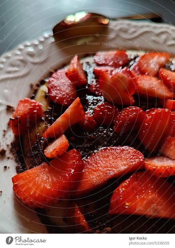 Closeup of full plate with porridge and fresh cut strawberries, sprinkled with cocoa powder, on a black table with golden spoon. food fruit red tasty juicy