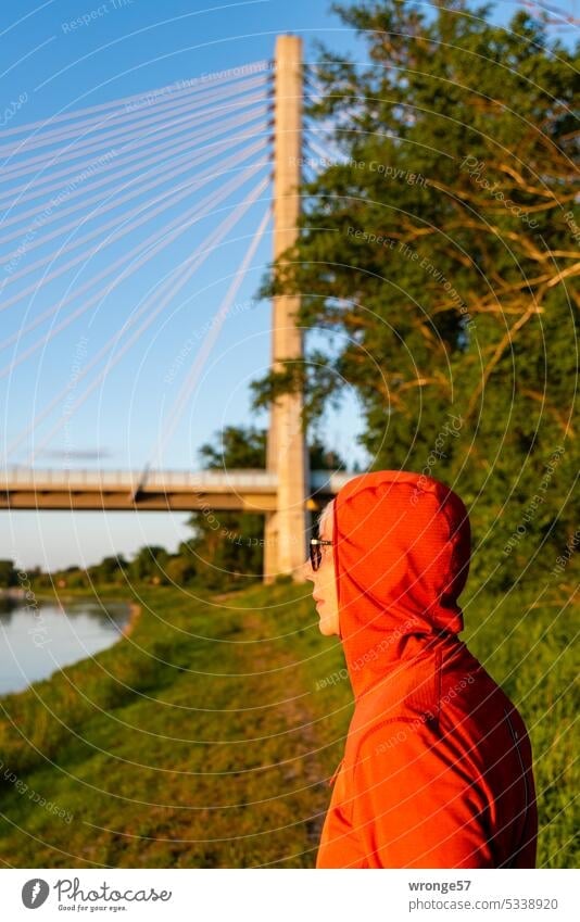 A woman wearing a red hooded jacket stands on the left bank of the Elbe near Schönebeck and looks out over the river Woman red jacket Profile River