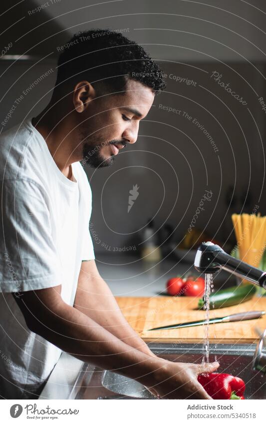 Ethnic man washing bell pepper during cooking preparation kitchen sink water prepare vegetarian fresh healthy food casual focus tap housework young vegetable