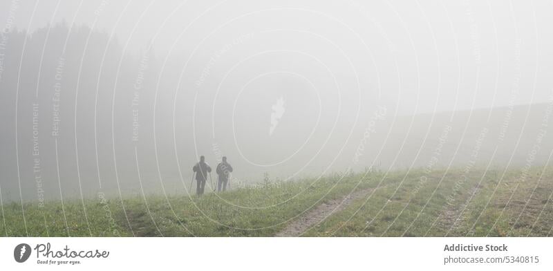 Anonymous people walking in foggy meadow nordic walk nature field landscape mist thick sport healthy wellness well being weather countryside grass rural rustic