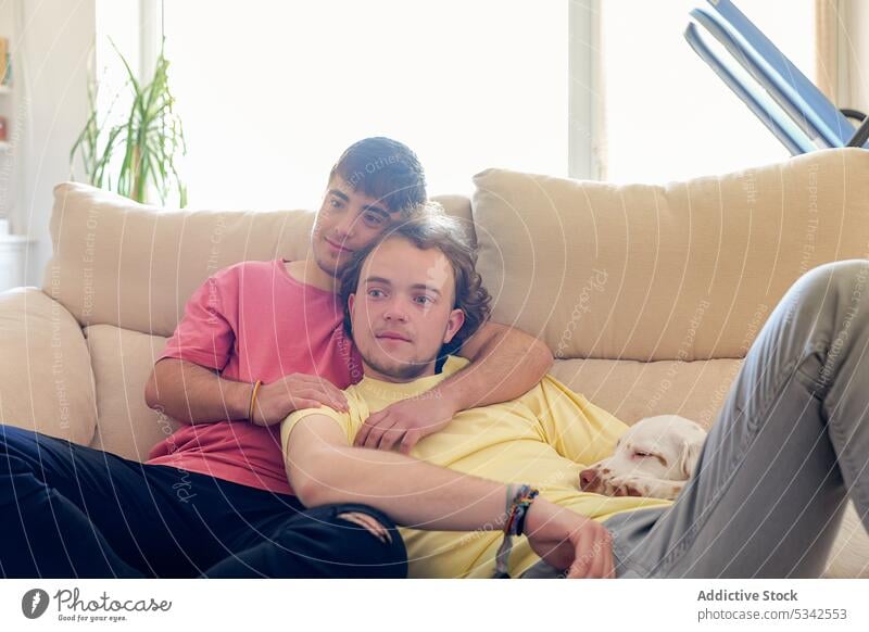 Gay couple hugging very intimate on the couch gay men dog sofa together rest transgender homosexual male home pet lgbt friend embrace relax living room lgbtq