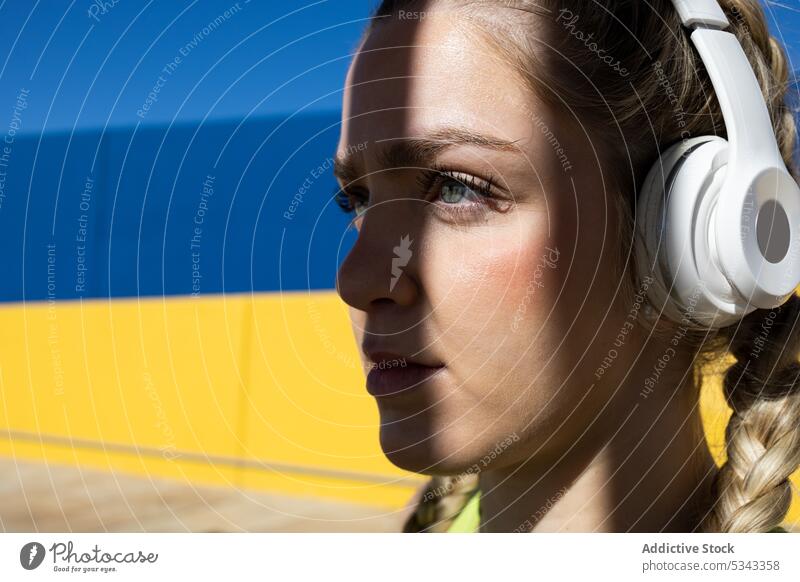 Young woman listening to music in headphones portrait braid confident shadow color wall calm young female bright vivid emotionless style colorful yellow trendy