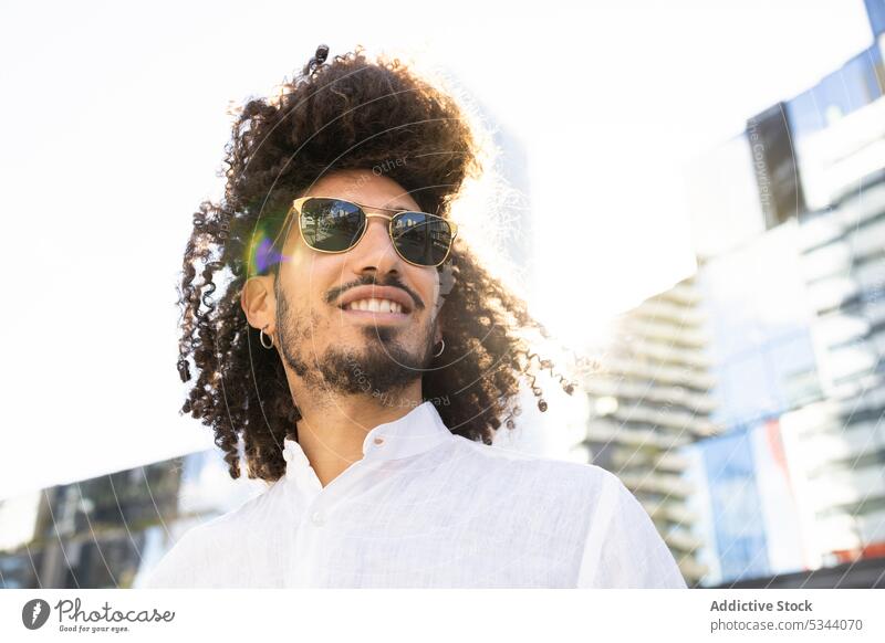 Ethnic smiling man with glasses on the street browsing trendy city sunglasses using device ethnic male black african american style masculine outfit urban